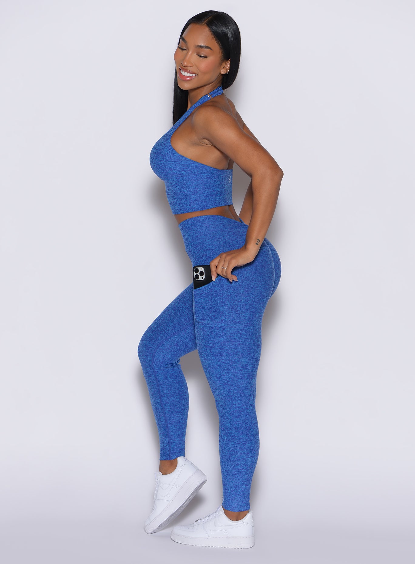 left side profile picture of a model smiling and wearing our V back leggings in Neon blue rave color along with a matching bra