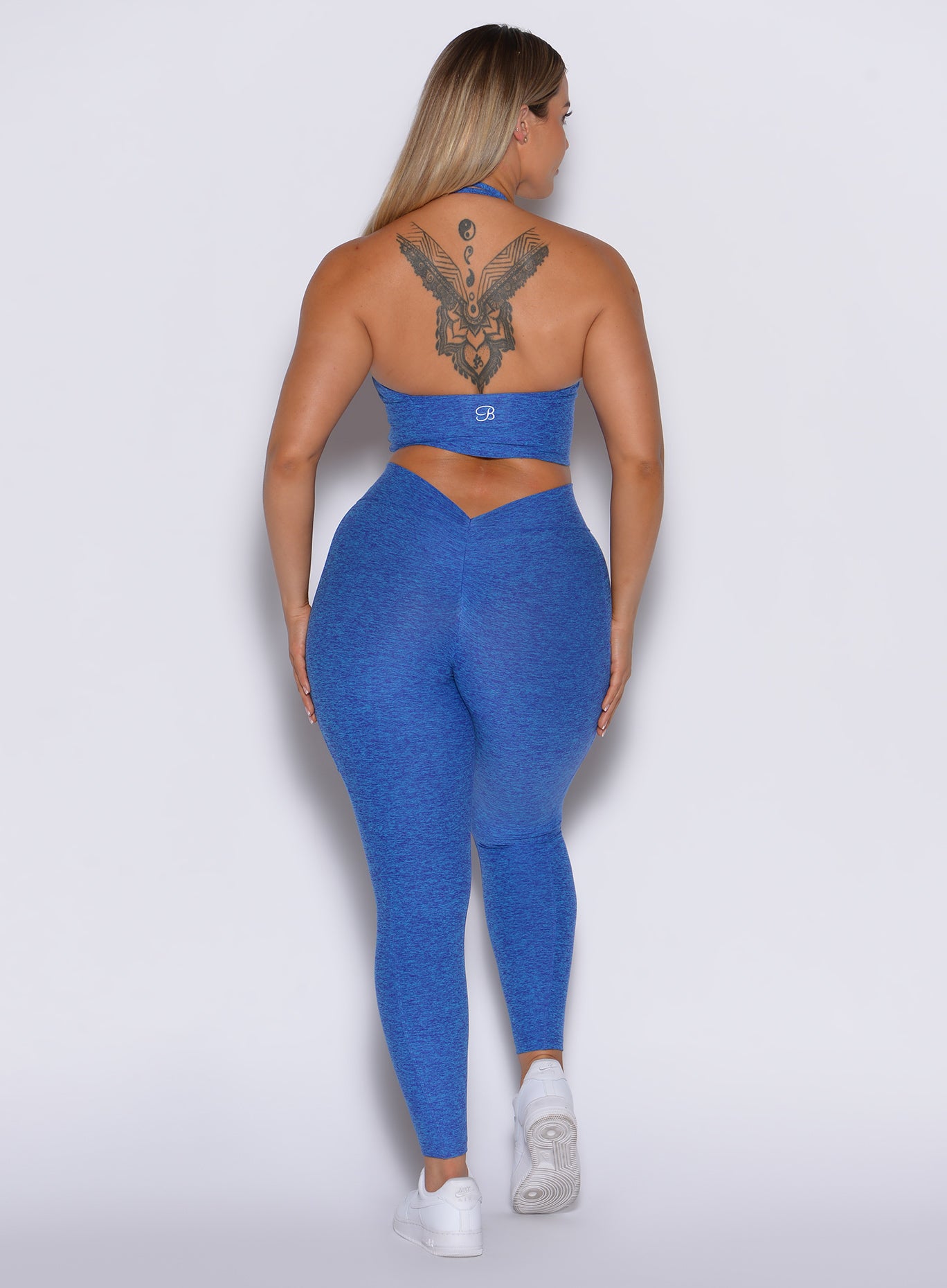 back profile view of a model wearing our V back leggings in Neon blue rave color along with a matching bra