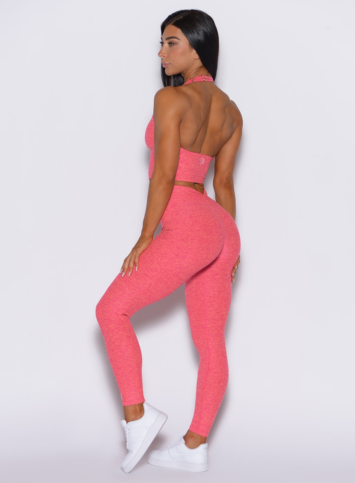 Left side profile view of a model wearing our V back leggings in Neon Tangerine Shock color along with a matching bra   