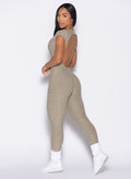 left side profile view of a model looking over her shoulder wearing the Open Back Tee Bodysuit in Toasted Sugar color