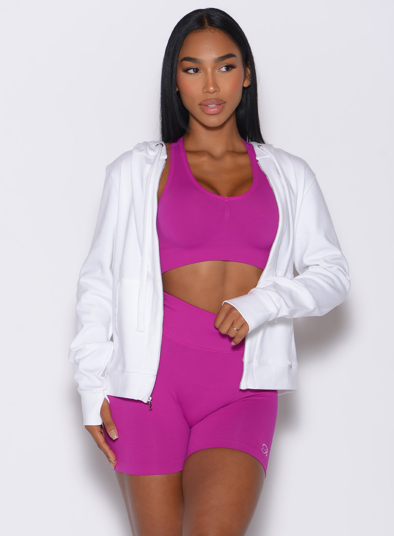 Front profile view of a model wearing our white oversized hoodie, along with shorts and a bra in berry color