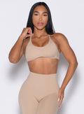 front profile view of a model holding the bra strap on the right side wearing the Passion Sports Bra in glacial beige color