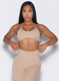 front profile view of a model adjusting the waistband of the leggings wearing the Passion Sports Bra in glacial beige color