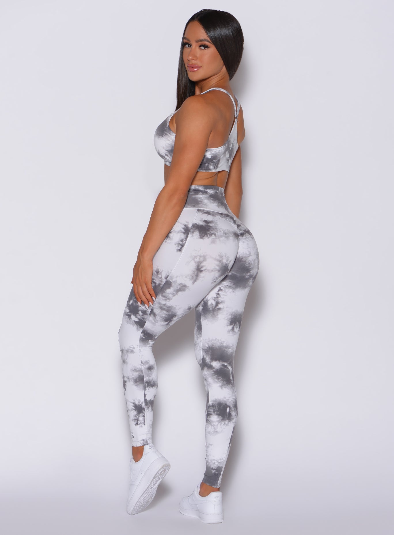 Left side profile picture of a model facing to her left wearing our tie dye peach booty leggings in gray white along with a matching bra 