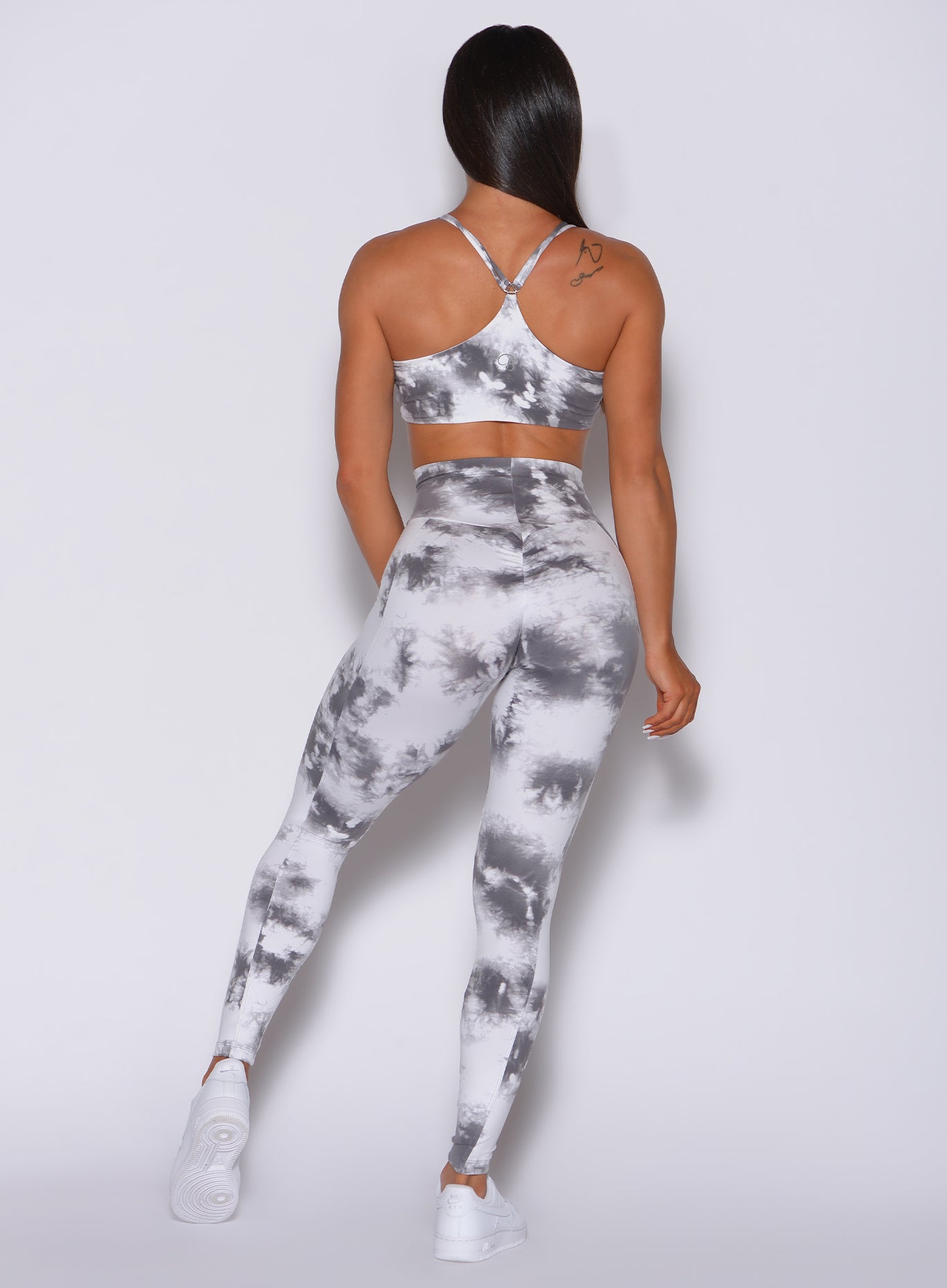Back side profile view of a model in our tie dye peach booty leggings in gray white and a matching sports  bra