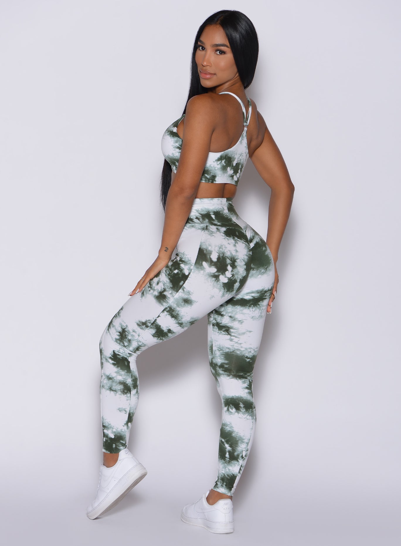 Left side profile view of a model facing to her left wearing our tie dye peach booty leggings in green white and a matching bra