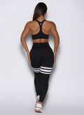 Back profile view of a model wearing our  black perform thigh high leggings and a matching top 
