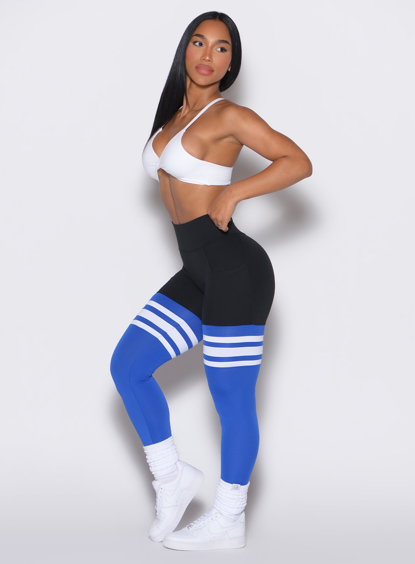 Left side profile view of a model wearing the Perform Thigh Highs in Black Sky color along with a white sports bra