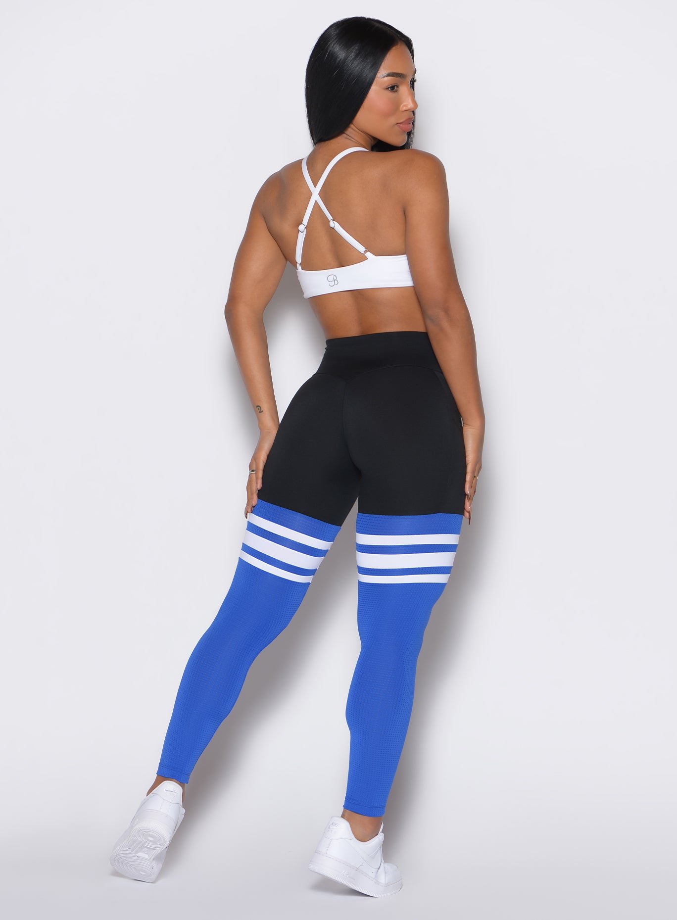 Back profile shot of a model  facing right wearing the Perform Thigh Highs in Black Sky color along with a white sports bra