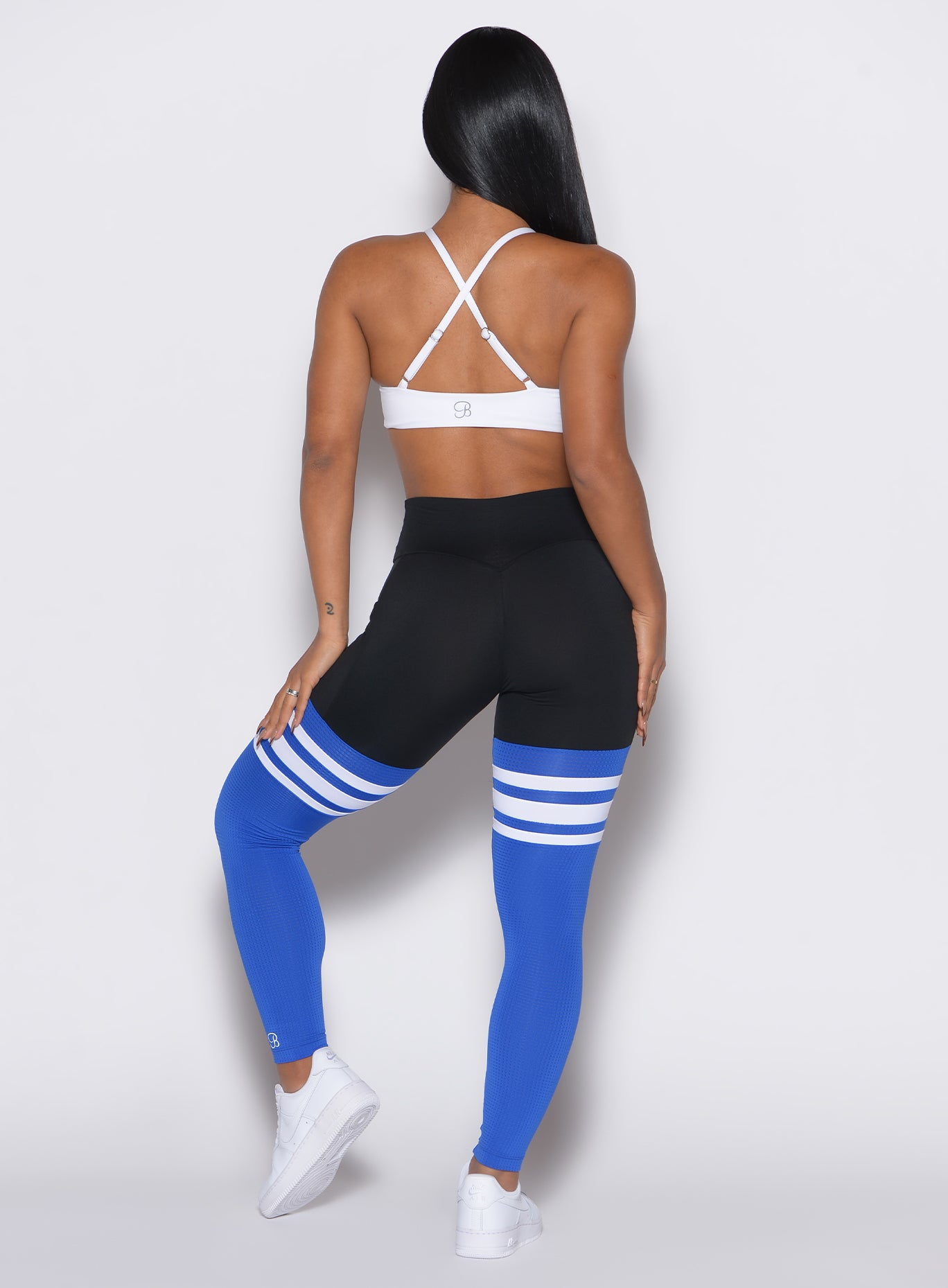 Back profile view of a model wearing the Perform Thigh Highs in Black Sky color along with a white sports bra
