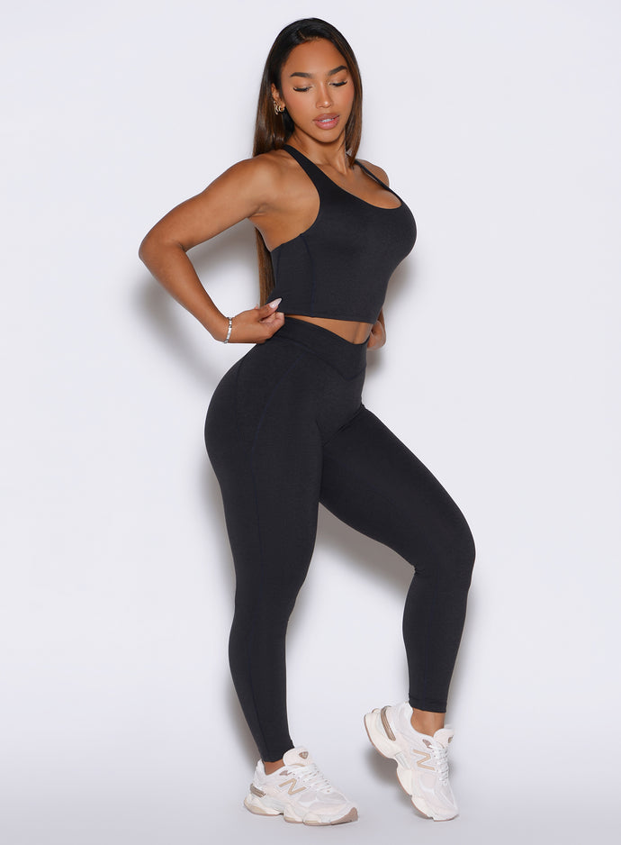 Front right side view of the model wearing our Physique leggings in Heathered Black color, while adjusting the matching top.
