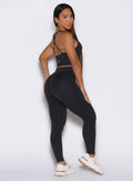 Back right side profile view of the model looking over her shoulder, wearing our Physique leggings in Heathered Black color.