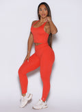 Front left side profile view of the model wearing our Physique leggings in Inferno, adjusting the strap of the matching top.