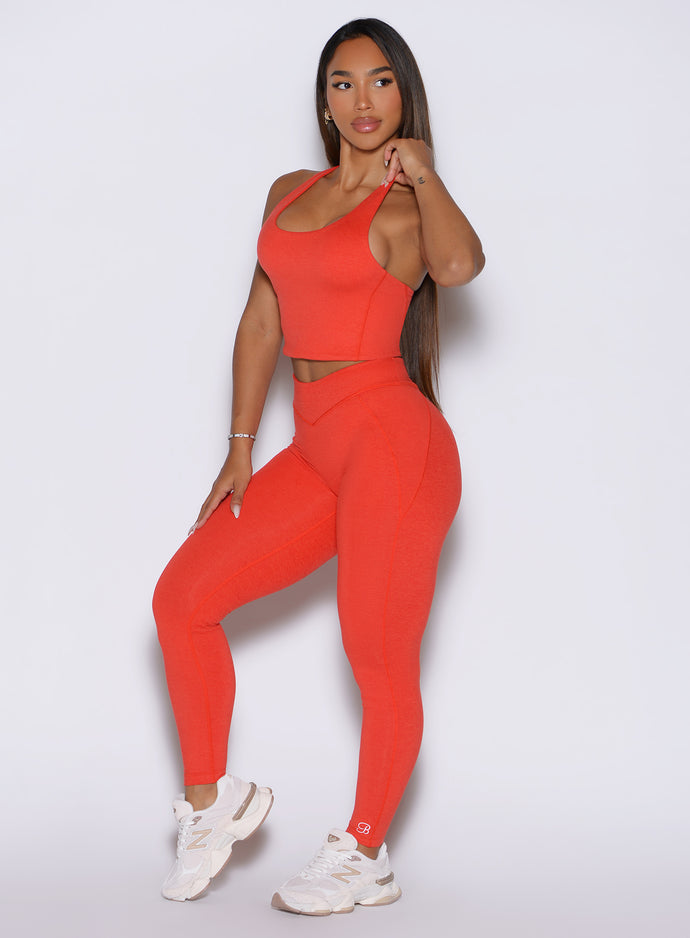 Front left side profile view of the model wearing our Physique leggings in Inferno, adjusting the strap of the matching top.