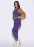 Left side profile view of the model wearing our Physique leggings in Iris color and adjusting the matching top.