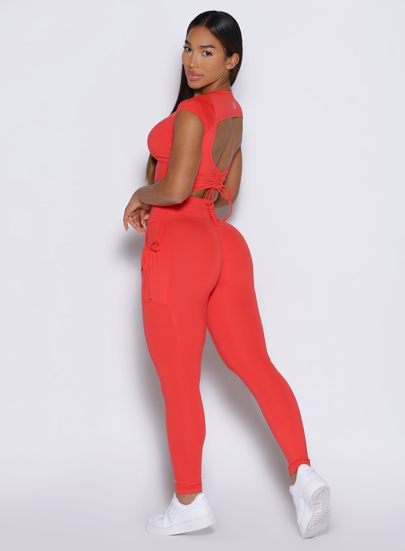 left side profile view of a model looking over her shoulder wearing the PocketBoost Leggings in Command red color