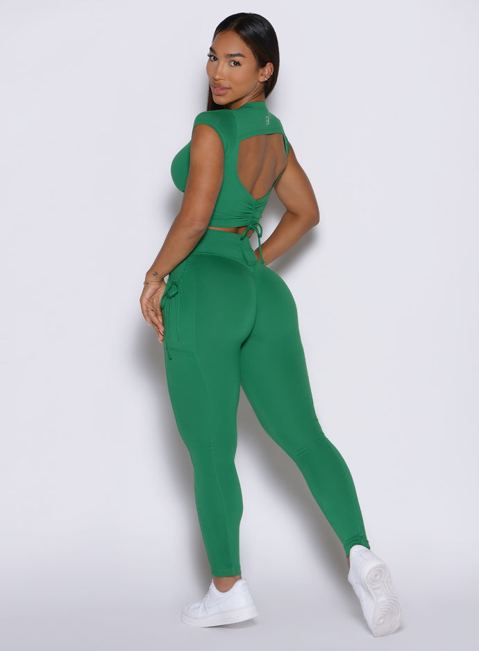back left side profile view of a model looking over her shoulder wearing the PocketBoost Leggings in Field Green color