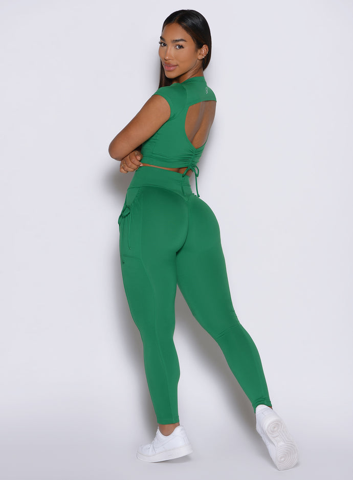 left side profile view of a model looking over her shoulder wearing the PocketBoost Leggings in Field Green color