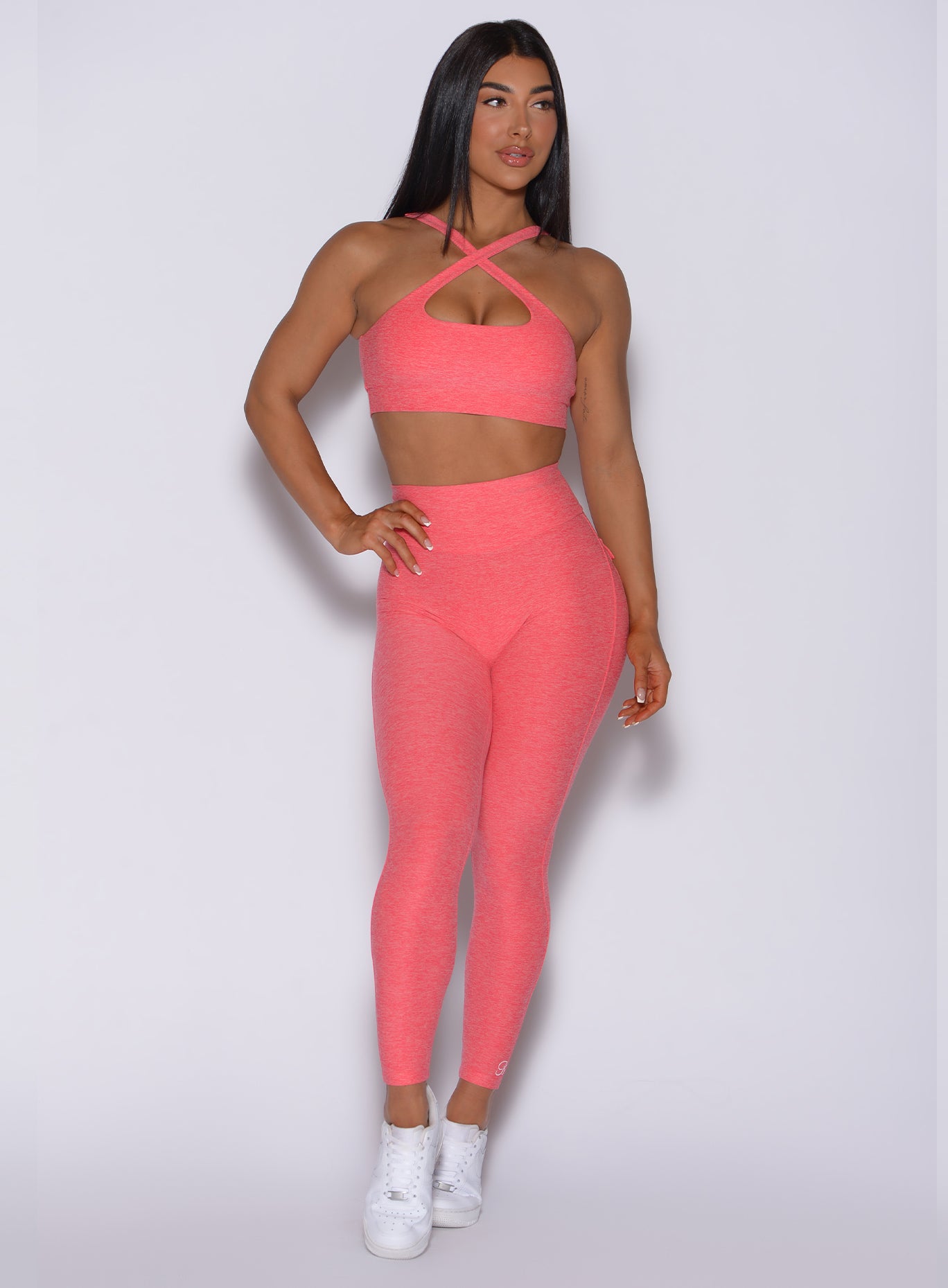 Front profile view of a model in our Pocket Pop Leggings in papaya color and a matching two way bra