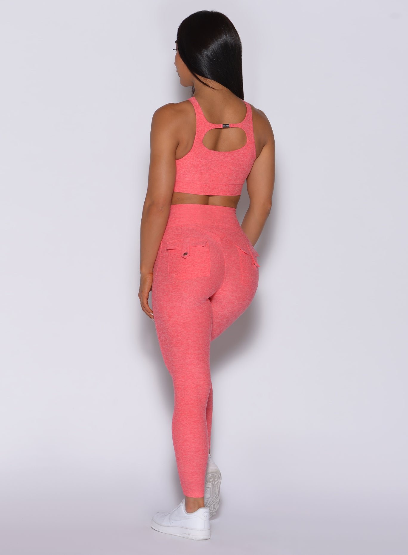 back profile view of a model in our Pocket Pop Leggings in papaya color and a matching two way sports bra