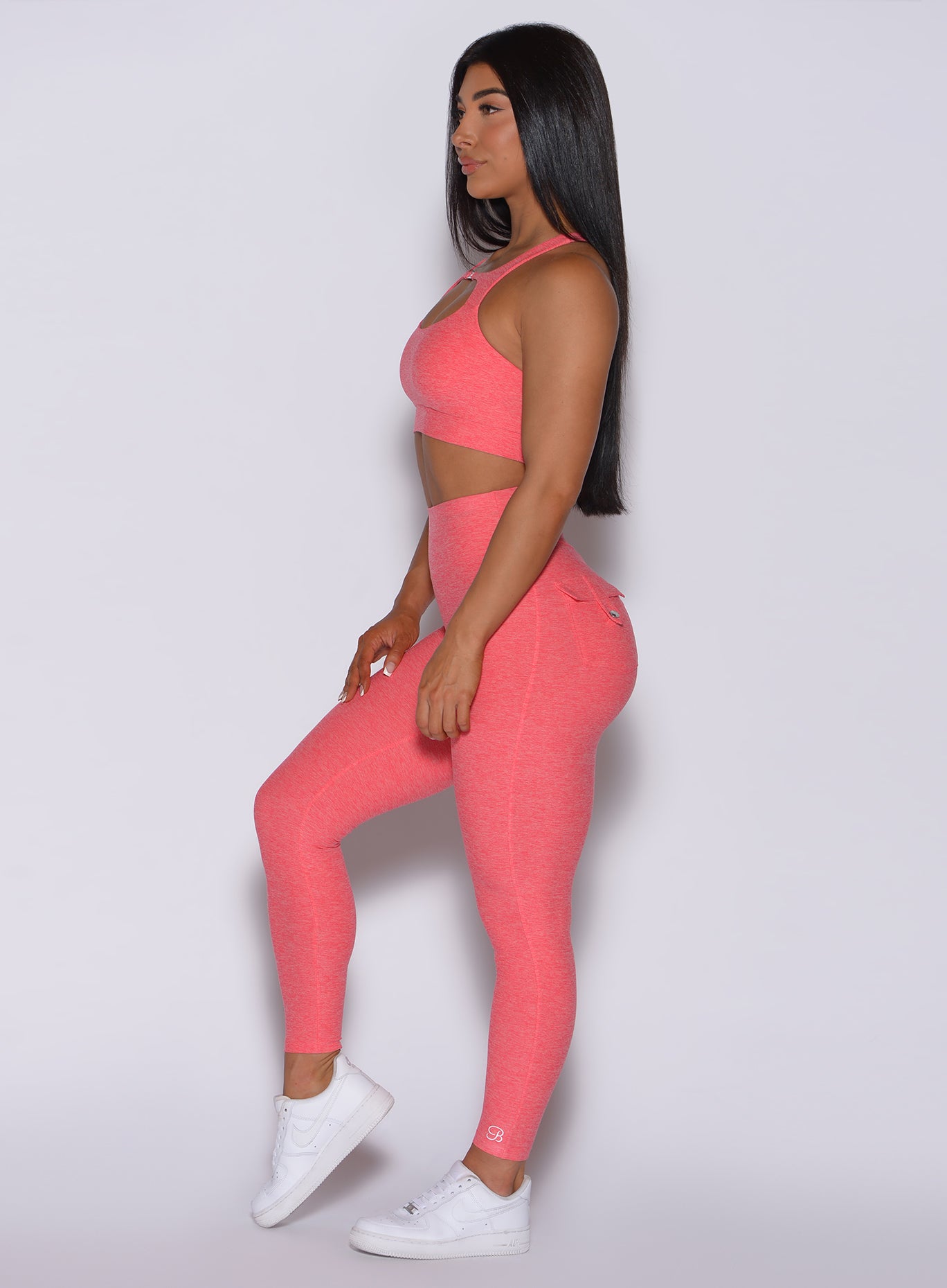 Left side profile view of a model in our Pocket Pop Leggings in papaya color and a matching bra
