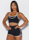front profile view of a model with both hands on her waist wearing the Power Line Bra in black color paired with the matching shorts 