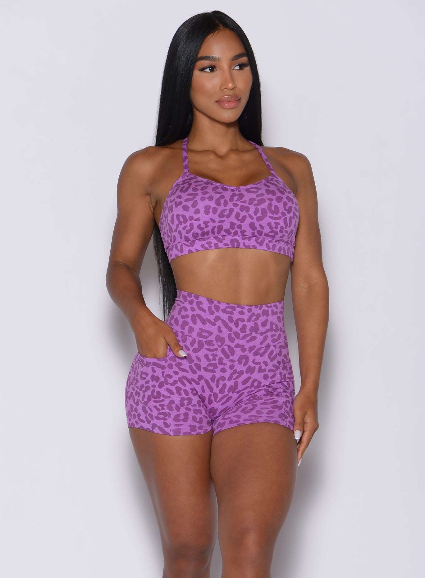 Front profile view of a model with her right hand in pocket wearing our pumped sports bra in purple cheetah color and matching shorts