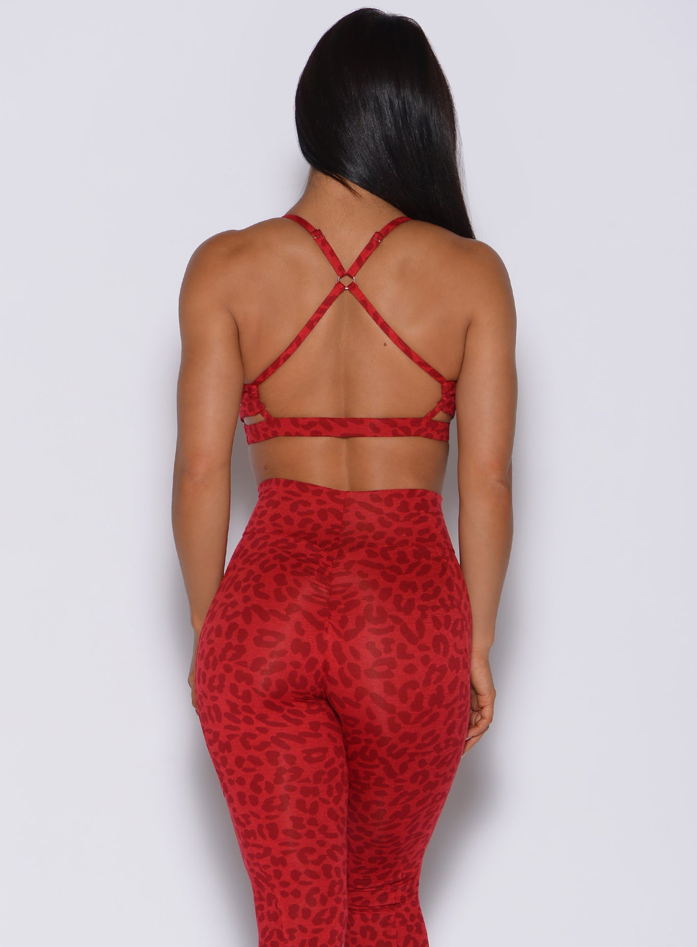 Back profile view of a model in our pumped sports bra in red cheetah color and matching leggings