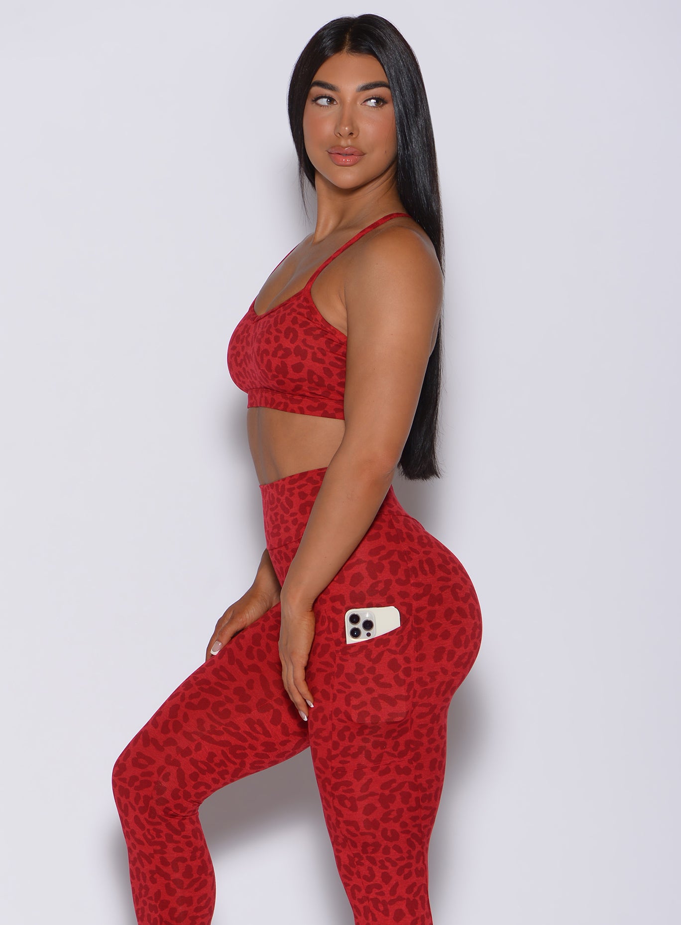 Left side profile view of a model in our pumped sports bra in red cheetah color and matching leggings