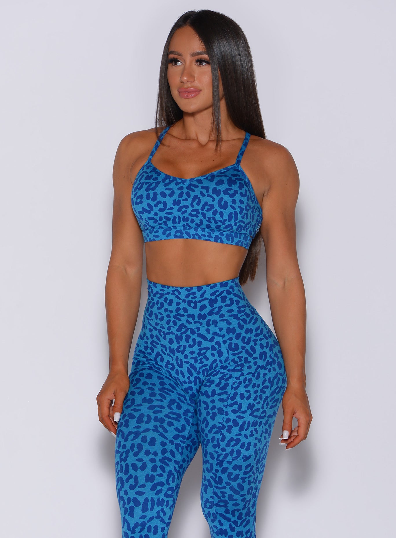 Front profile view of a model looking to her right wearing our pumped sports bra in blue cheetah color and matching leggings