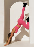 model in an upside down pose supporting herself with the legs on a wall wearing the Electric Era Top in neon flame color paired with the matching leggings