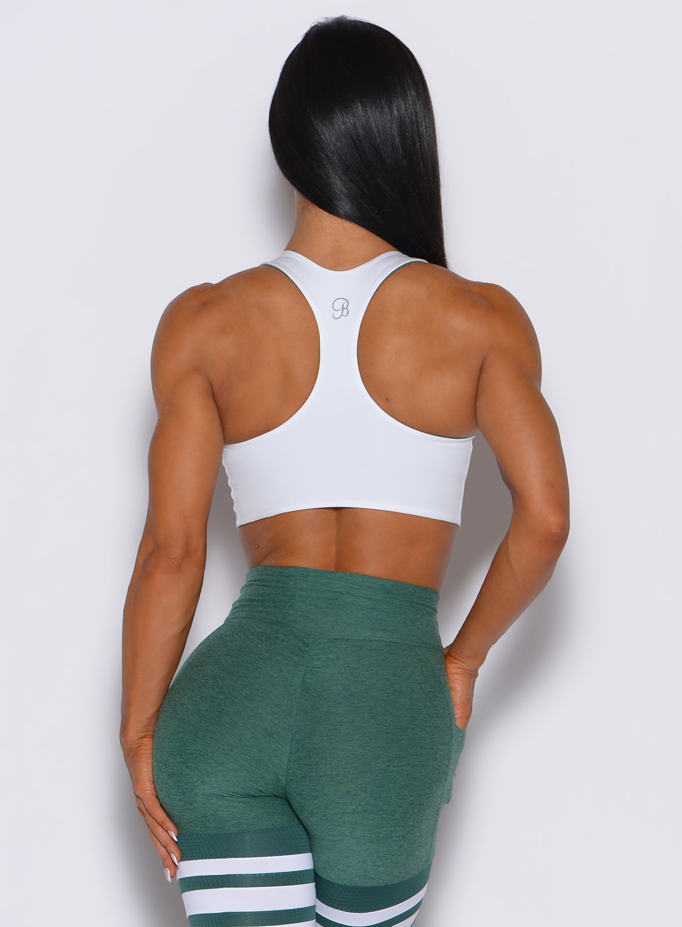 Back profile view of a model wearing our white reversible tank bra along with a thigh high in emerald green color 