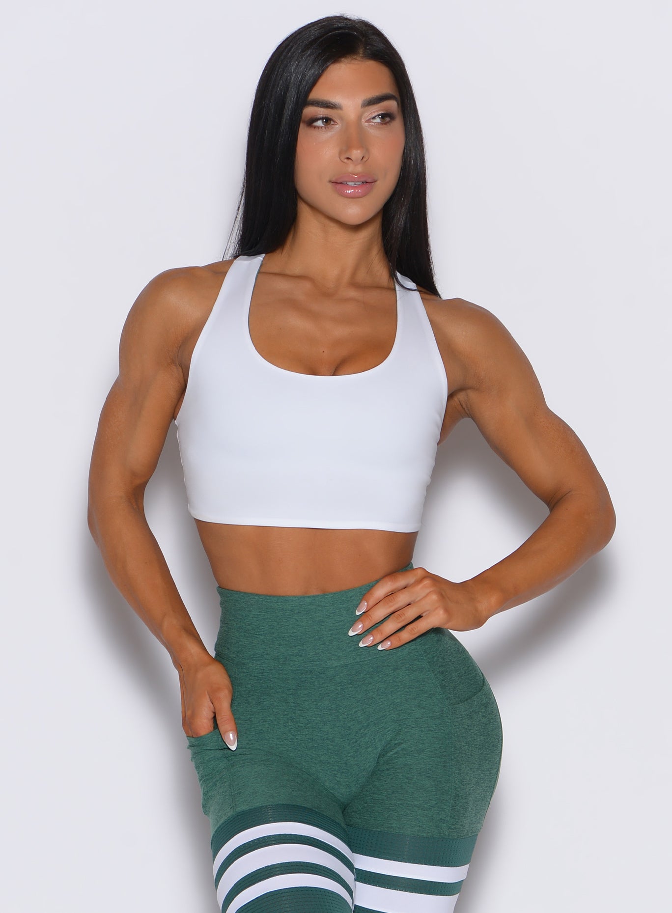 Front profile view of a model wearing our white reversible tank bra along with a leggings in emerald green color 