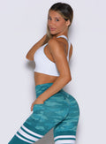 left side profile view of a model wearing the Reversible Tank Bra in Teal camo paired with the matching leggings 