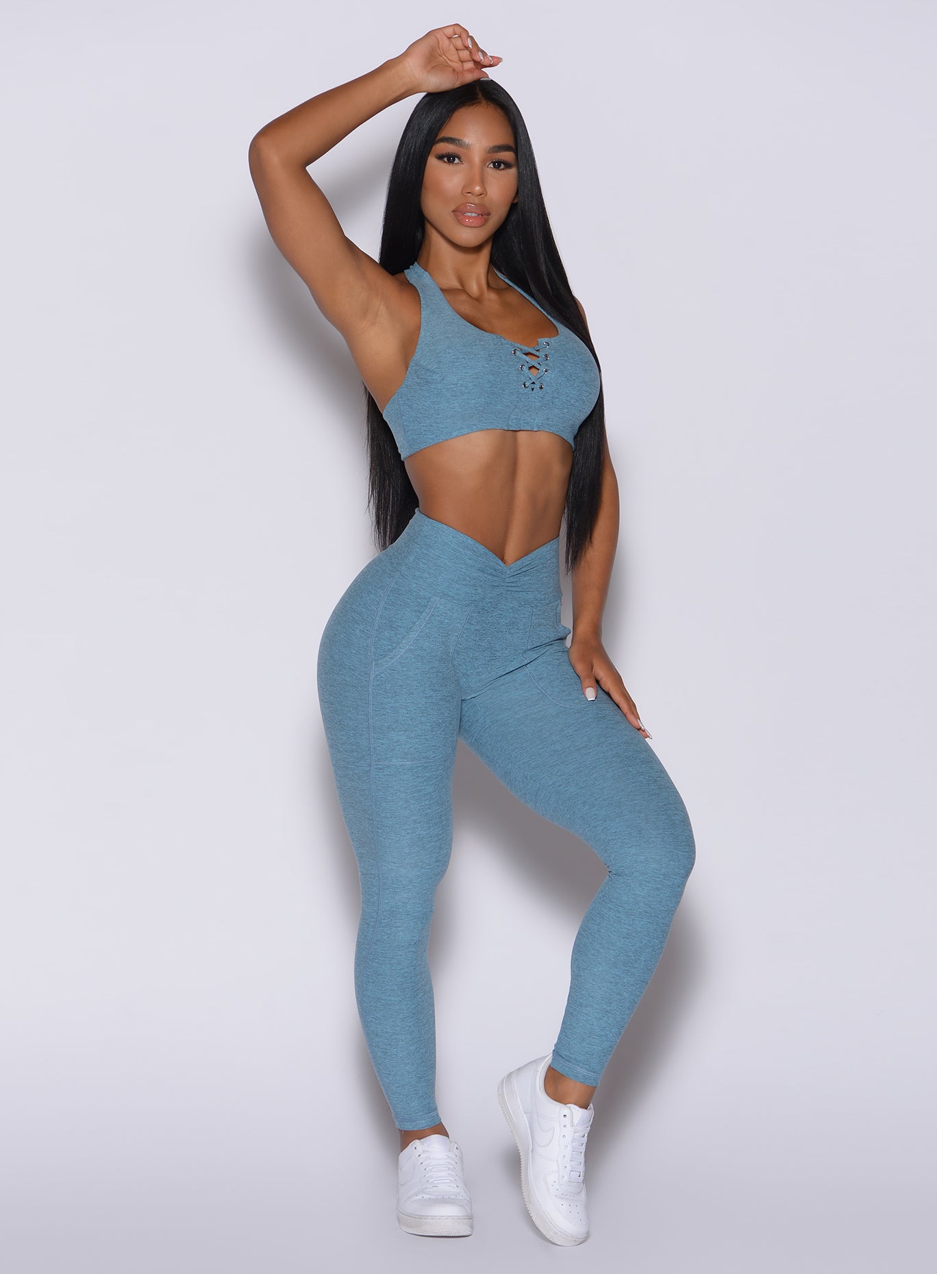 Front profile view of a model with her right hand over her head wearing our V scrunch leggings in baby blue color and a matching bra