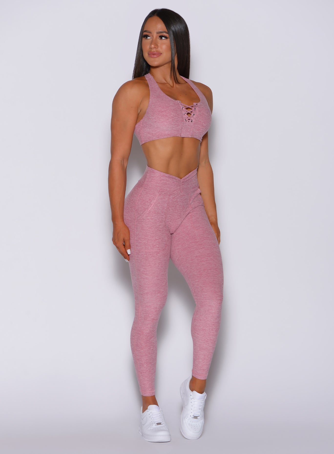 Front profile view of a model facing to her right wearing our V scrunch leggings in rose blush color and a matching bra