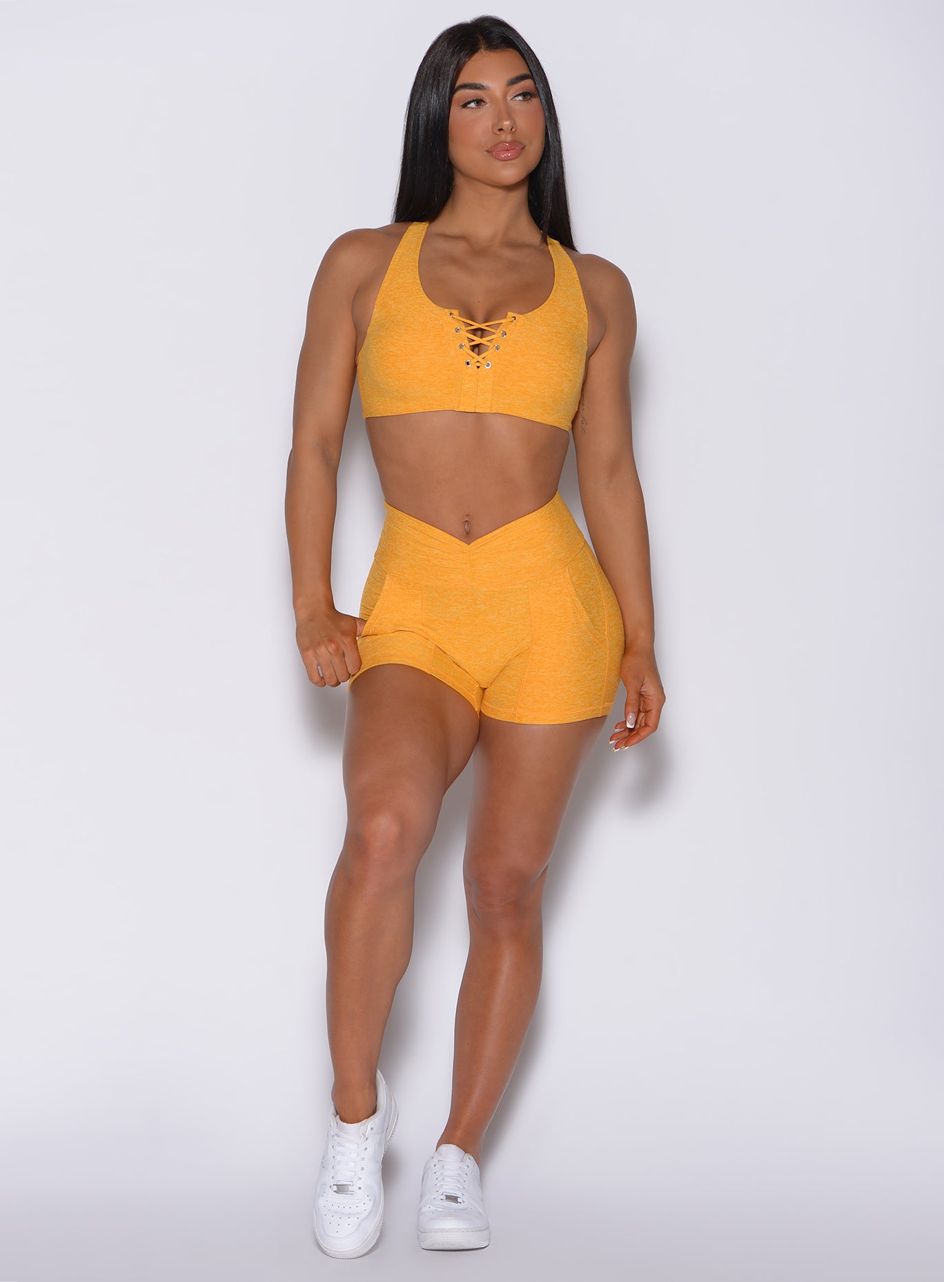 Front profile view of a model in our V scrunch shorts in sunkissed color and a matching bra 