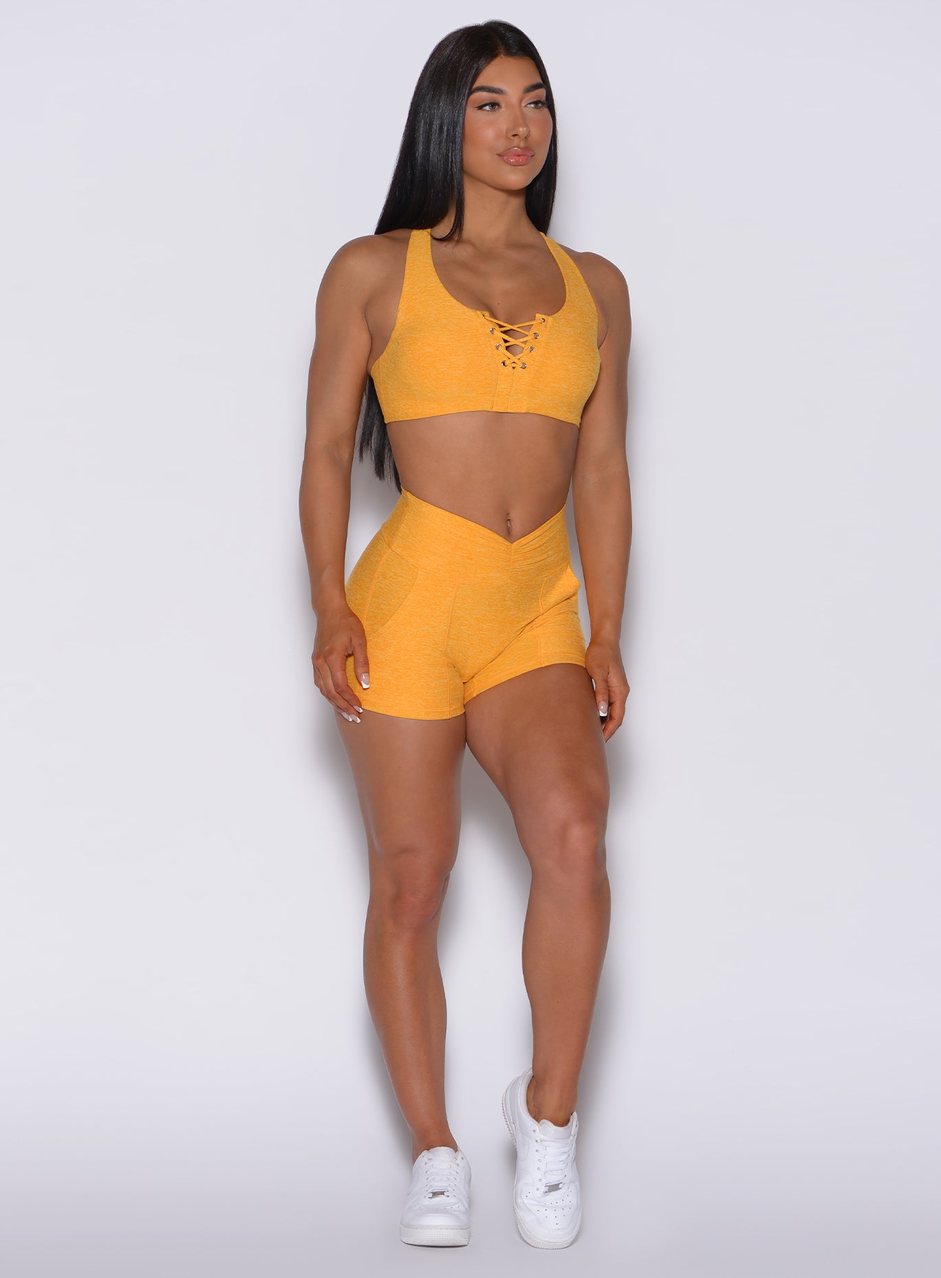 Front profile view of a model facing forward wearing our V scrunch shorts in sunkissed color and a matching bra