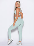 Left side profile view of our model looking over her shoulder wearing the Define Leggings in Mist color