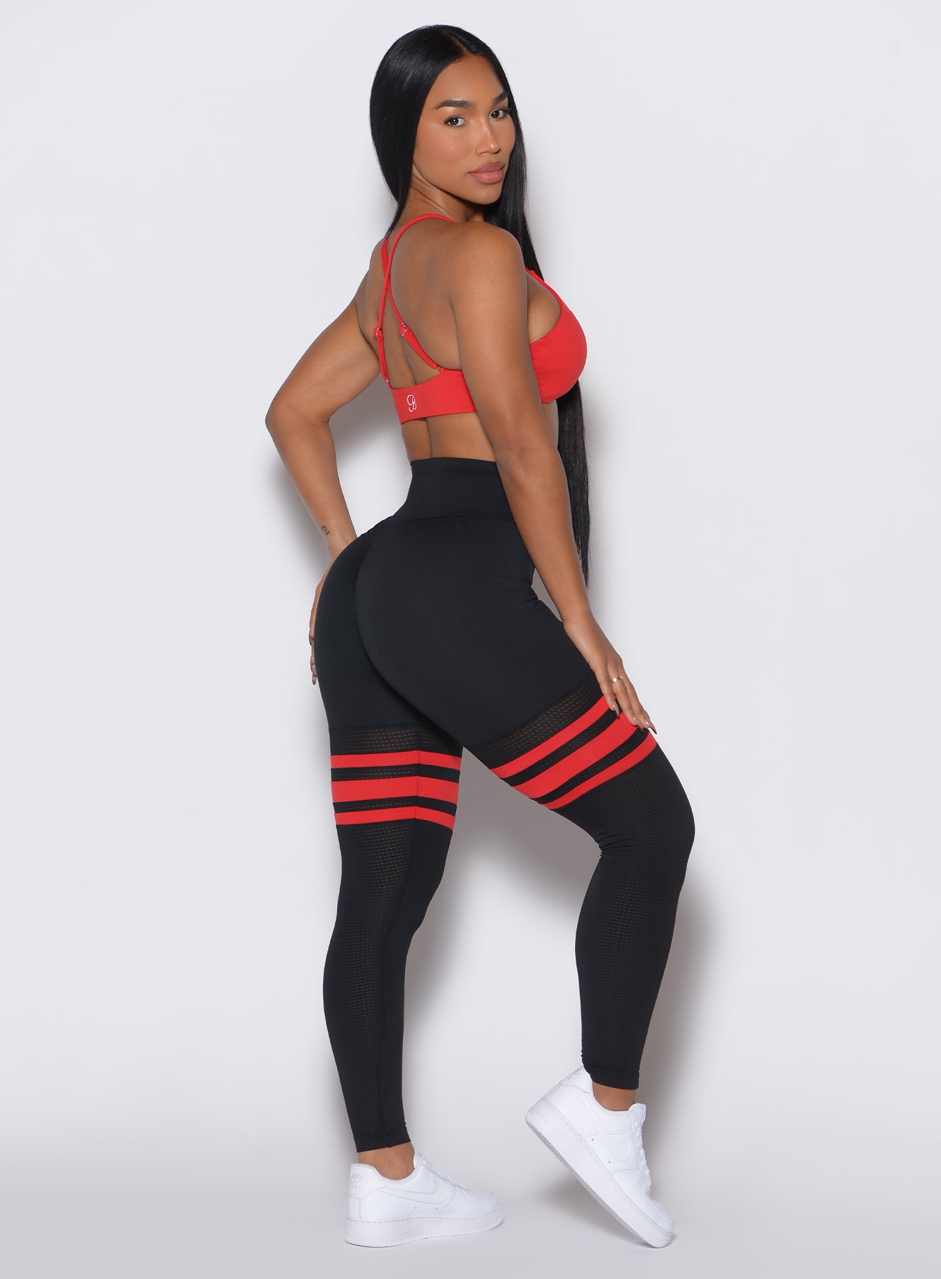 Right side profile view of a model facing to her right wearing our Scrunch Thigh Highs in Black Fire color along with a matching red sports bra 