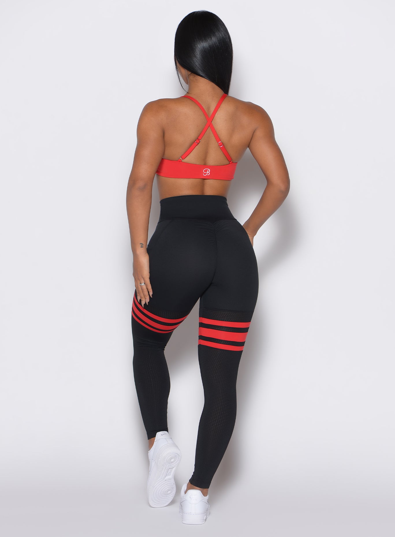 Back profile view of a model wearing the Scrunch Thigh Highs in Black Fire color along with a red sports bra