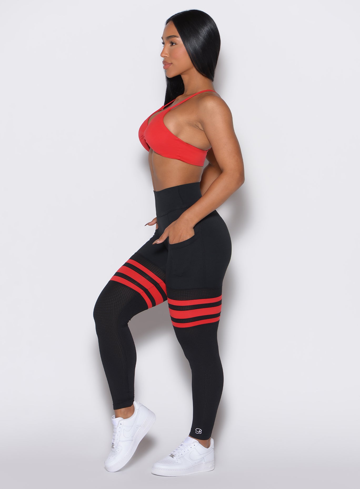 Left profile view of a model wearing the Scrunch Thigh Highs in Black Fire color along with a red sports bra  