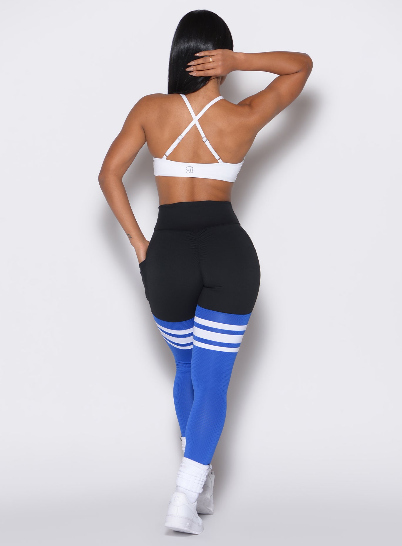 Back profile view of a model wearing our  scrunch thigh high in black and royal color along with a white sports bra 