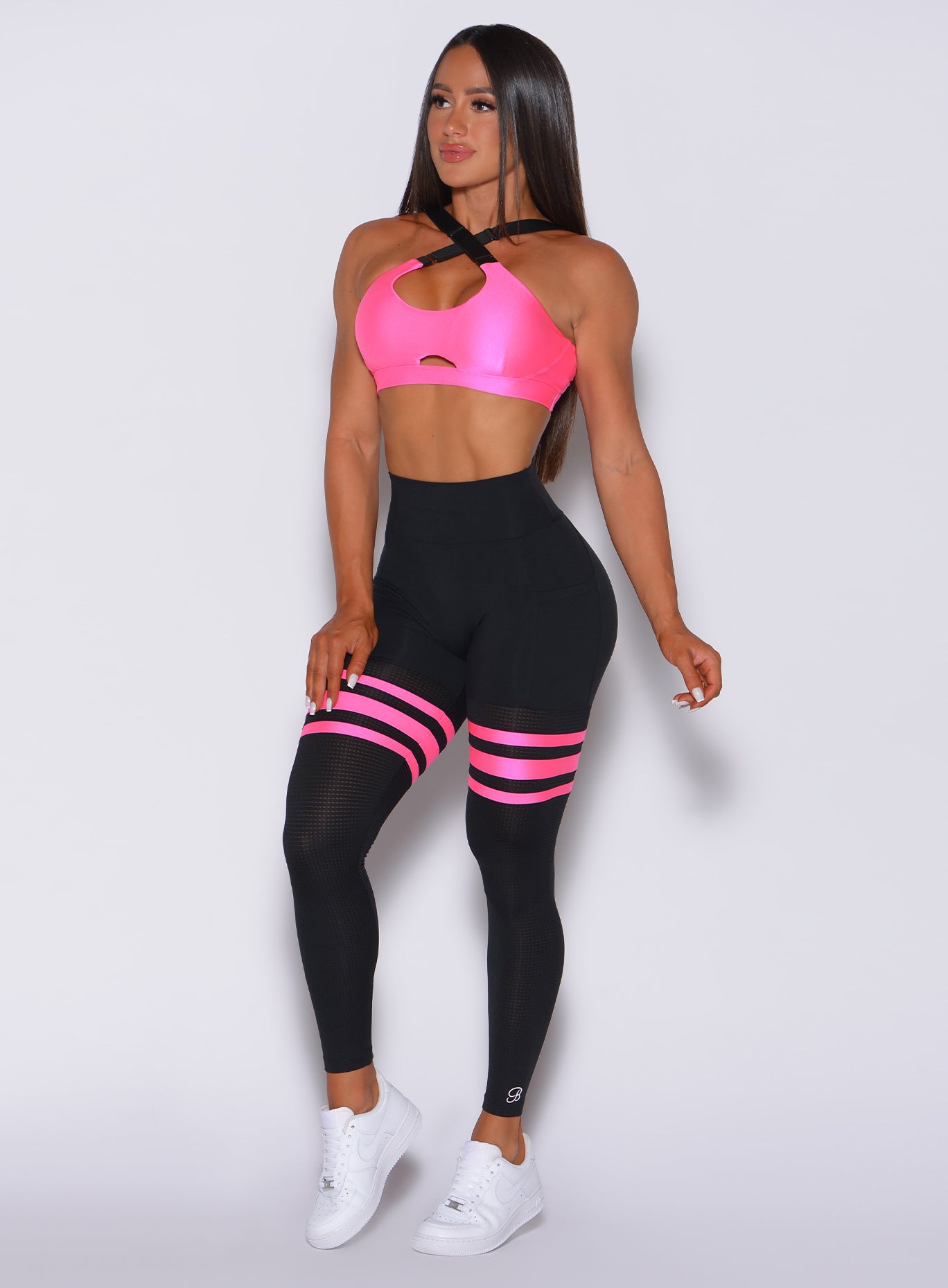 Front profile view of a model wearing our scrunch thigh high in black with neon pink stripes on the thighs and a matching sports bra