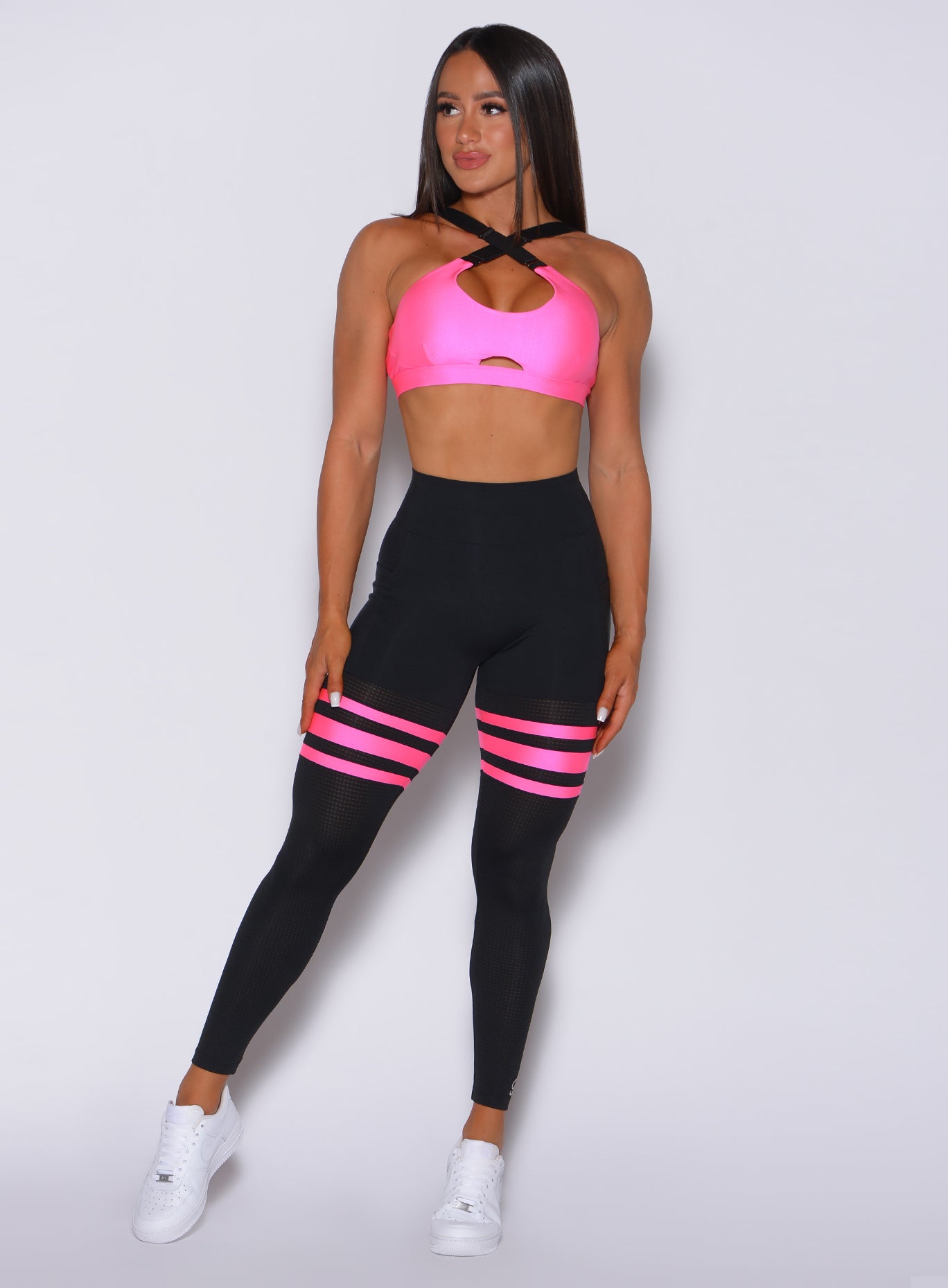 Front  profile view of a model in our black scrunch thigh high with neon pink stripes on the thighs and a matching sports bra
