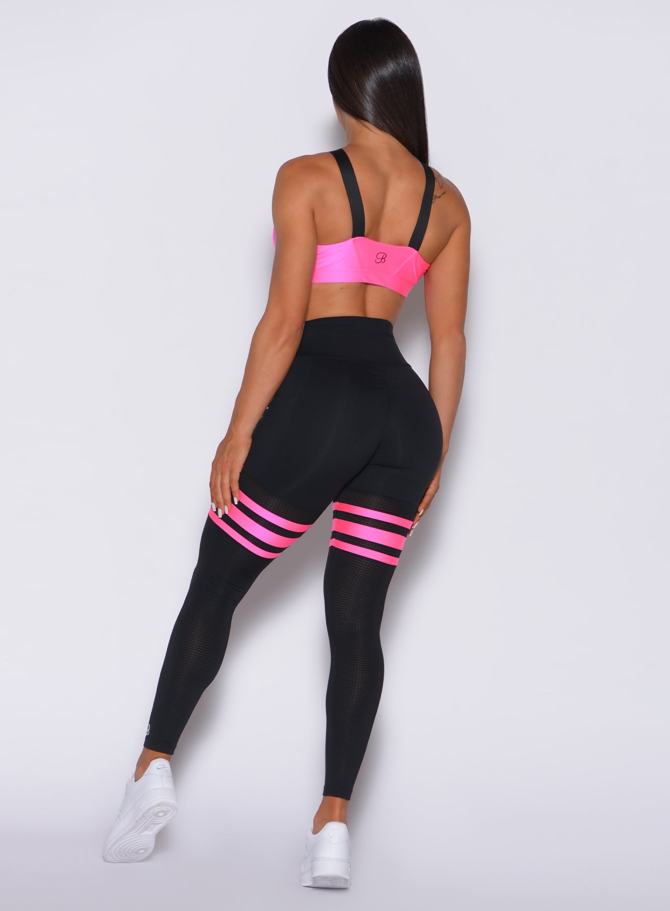 Back profile view of a model in our scrunch thigh high in black with neon pink stripes on the thighs and a matching sports bra
