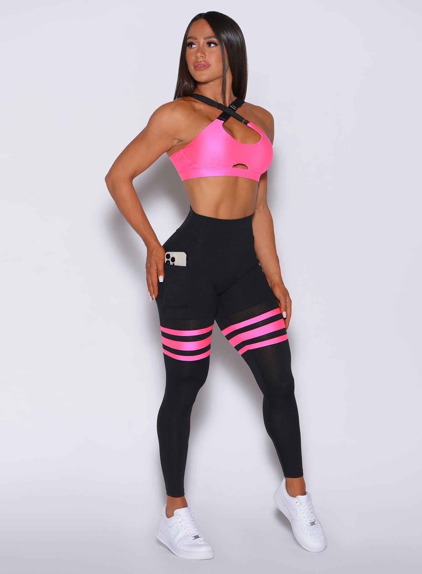 Right side profile view of a model angled to her right wearing our scrunch thigh high in black with neon pink stripes on the thighs and a matching sports bra