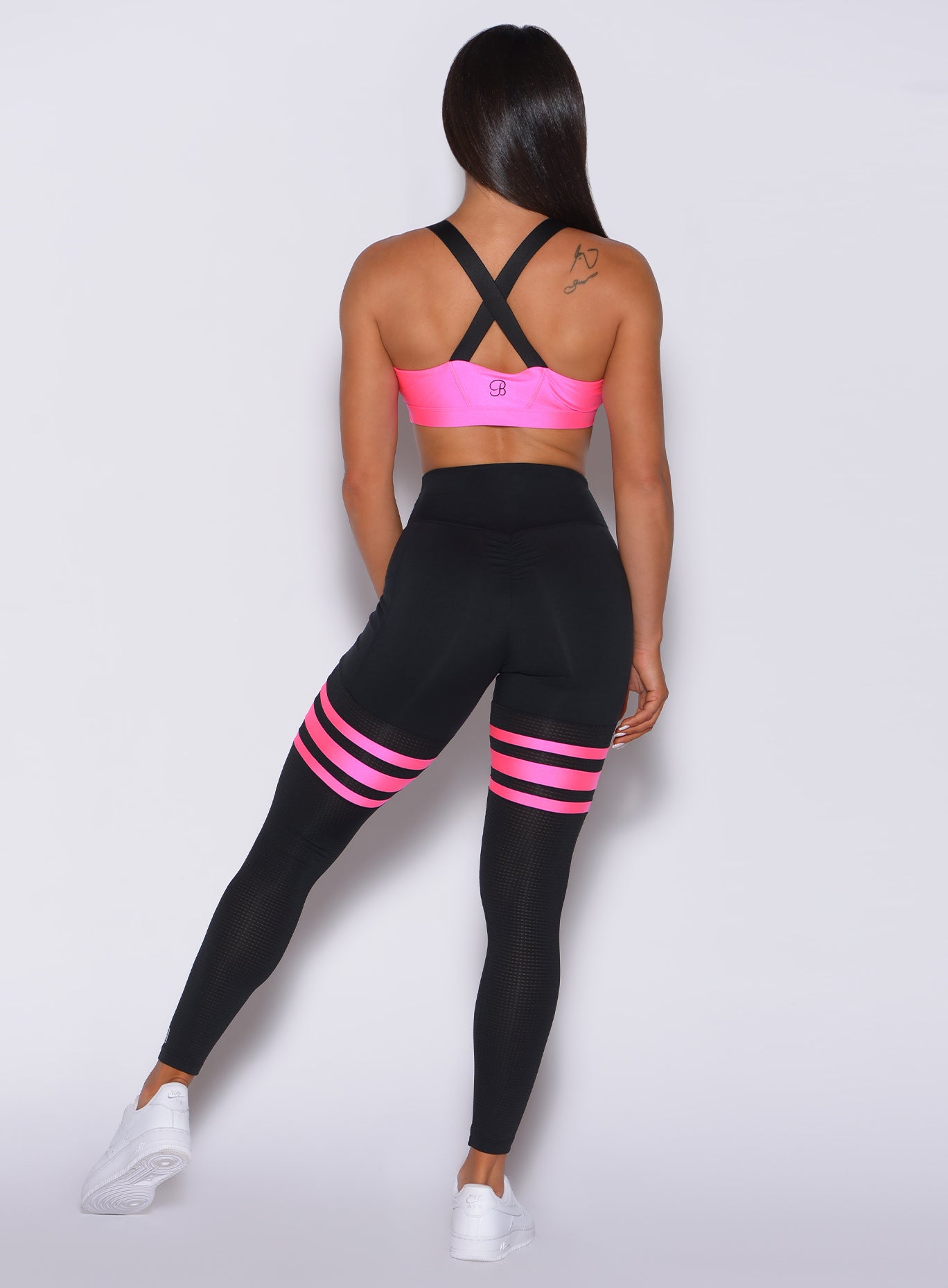 Back  profile view of a model in our black scrunch thigh high with neon pink stripes on the thighs and a matching sports bra