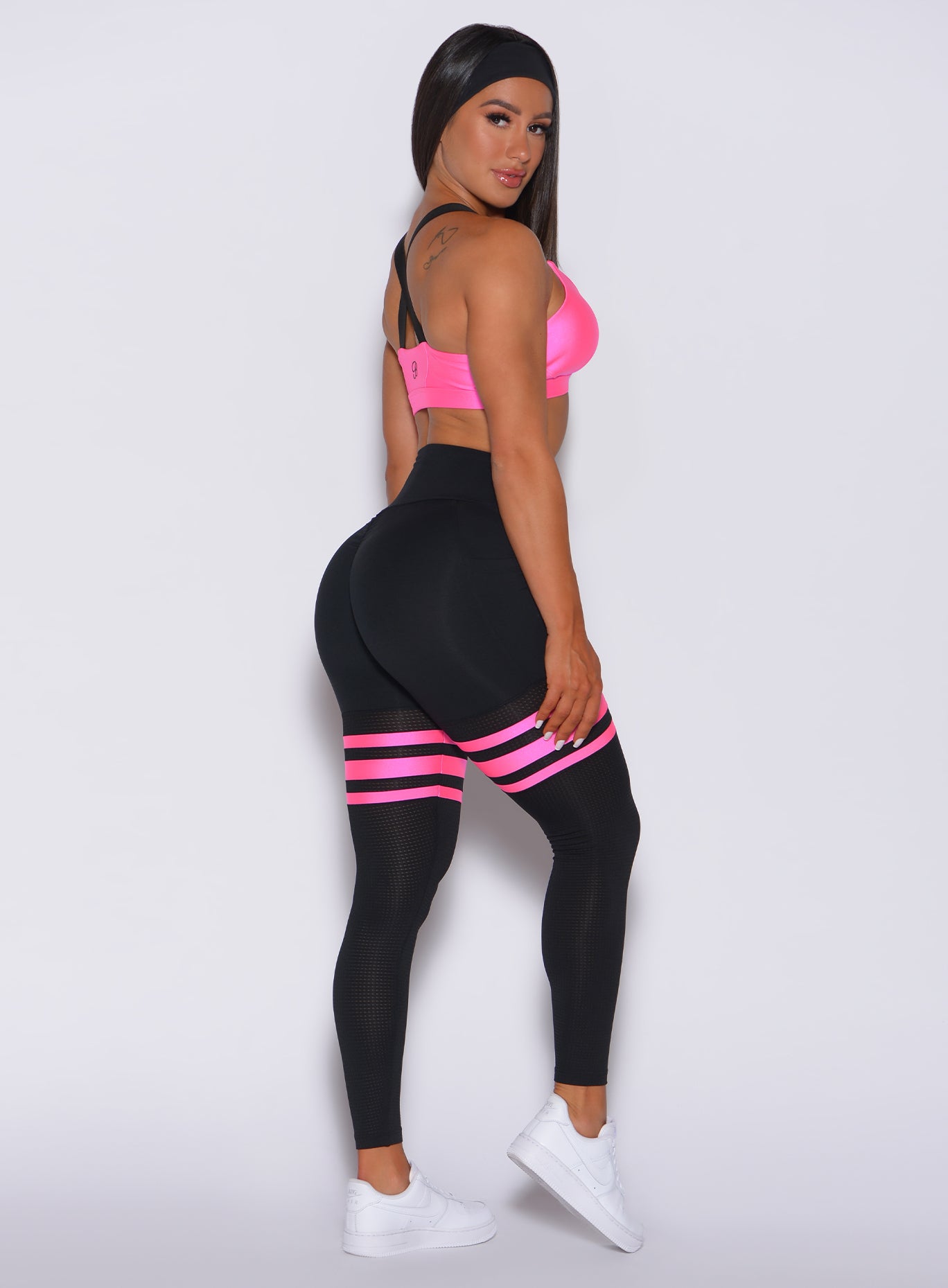 Right side profile view of a model facing to her right wearing our scrunch thigh high in black with neon pink stripes on the thighs and a matching glow sports bra