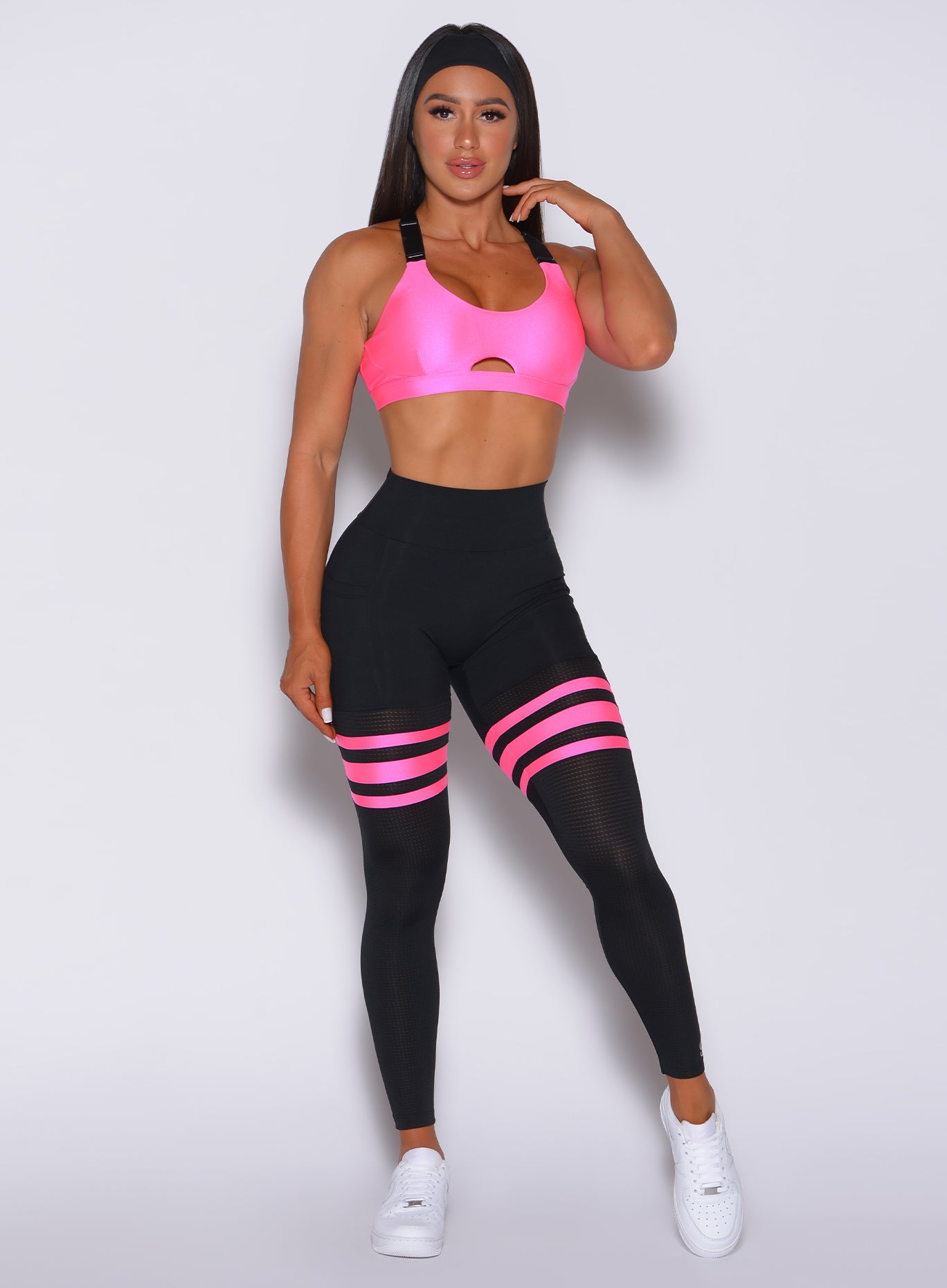 Front profile view of a model facing forward wearing our scrunch thigh high in black with neon pink stripes on the thighs and a matching sports bra